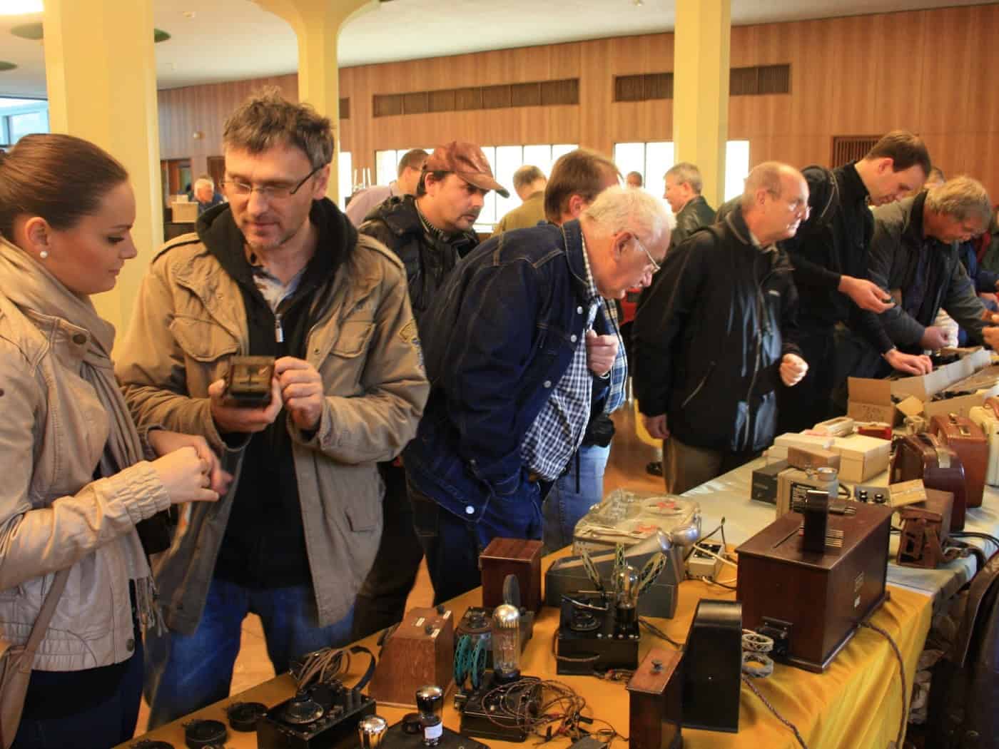 Besucher der AREB-Börse stehen an einem mit historischen Radios, Röhren und Holzgehäusen gefüllten Tisch im Foyer des Hauses der Presse und begutachten alte Elektronik.