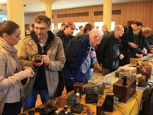 Besucher der AREB-Börse stehen an einem mit historischen Radios, Röhren und Holzgehäusen gefüllten Tisch im Foyer des Hauses der Presse und begutachten alte Elektronik.