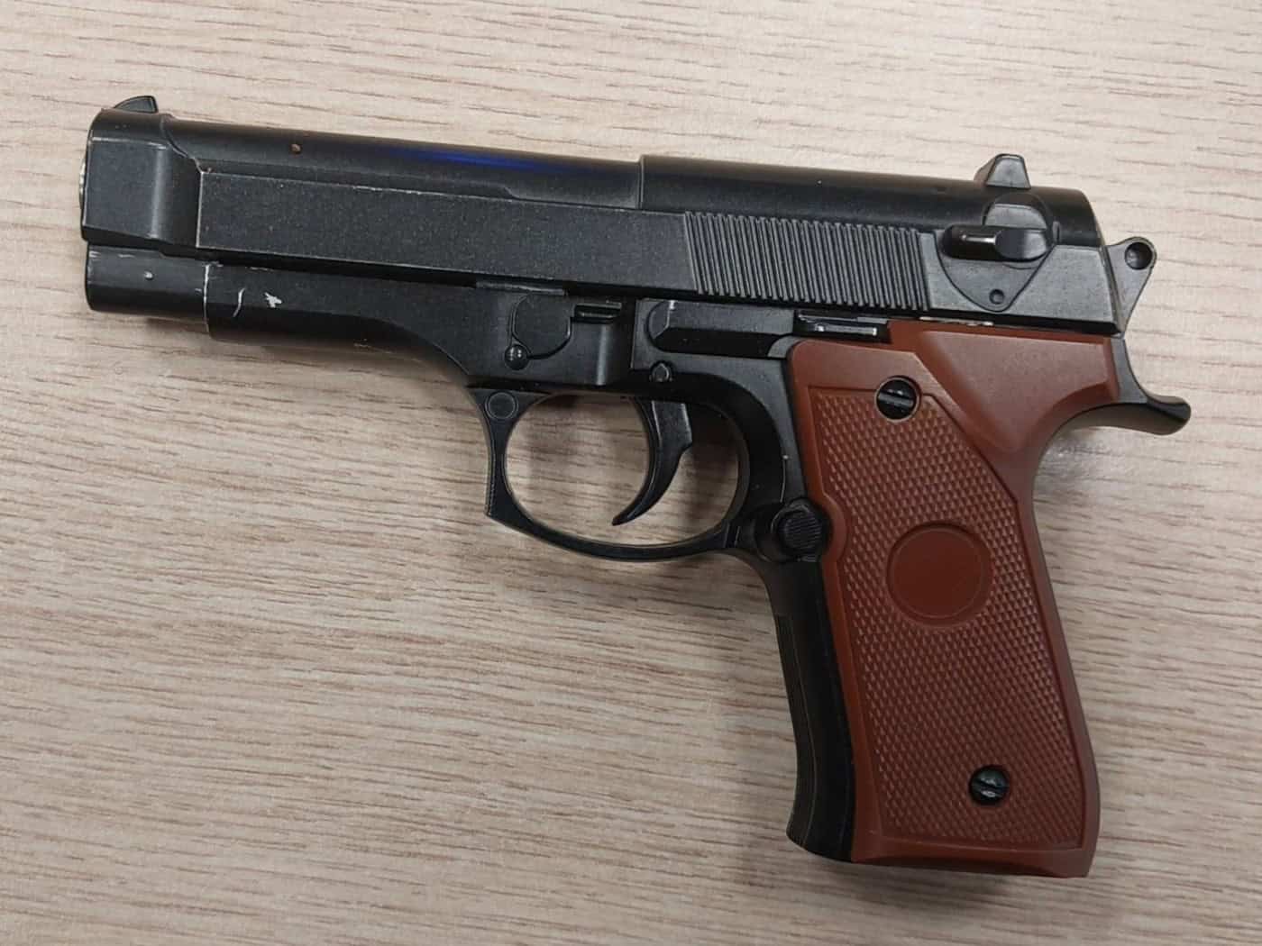 Eine schwarze Anscheinswaffe mit braunem Griffstück liegt auf einem hellen Holztisch. Die Pistole sieht einer echten Schusswaffe täuschend ähnlich und wurde bei Kontrollen der Bundespolizei an den Dresdner Bahnhöfen als Softairwaffe sichergestellt.