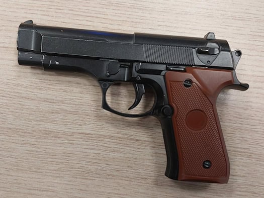 Eine schwarze Anscheinswaffe mit braunem Griffstück liegt auf einem hellen Holztisch. Die Pistole sieht einer echten Schusswaffe täuschend ähnlich und wurde bei Kontrollen der Bundespolizei an den Dresdner Bahnhöfen als Softairwaffe sichergestellt.
