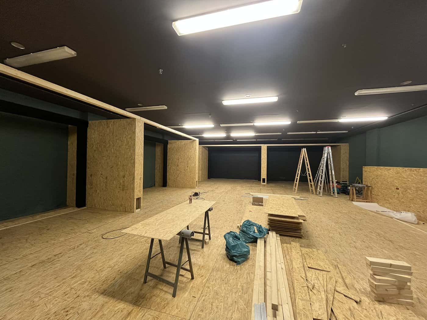 Blick in einen umgebauten Kinosaal im Bofimax Dresden mit Holzverkleidungen und OSB-Platten am Boden. Auf der Baustelle stehen Holzböcke, Platten und Leitern für den Aufbau der neuen Indoor-Golf-Simulatoren unter Leuchtstoffröhren.