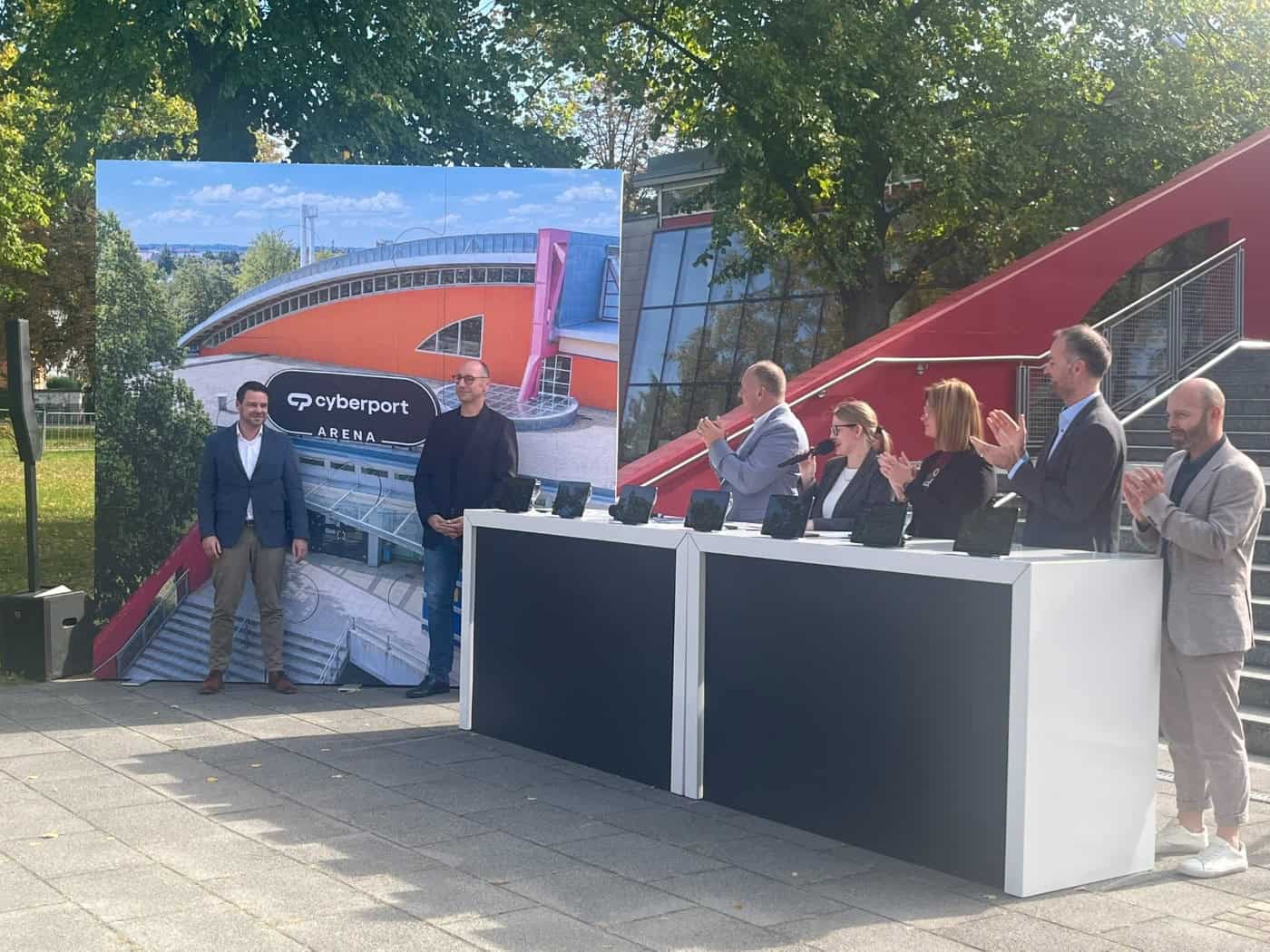 Offizielle Präsentation vor der Dresdner Arena: Links steht eine Fotowand mit der Abbildung der Sporthalle und dem neuen Schriftzug „cyberport ARENA“. Rechts klatschen Vertreter von Stadt und Sponsor an einem weißen Stehpult.