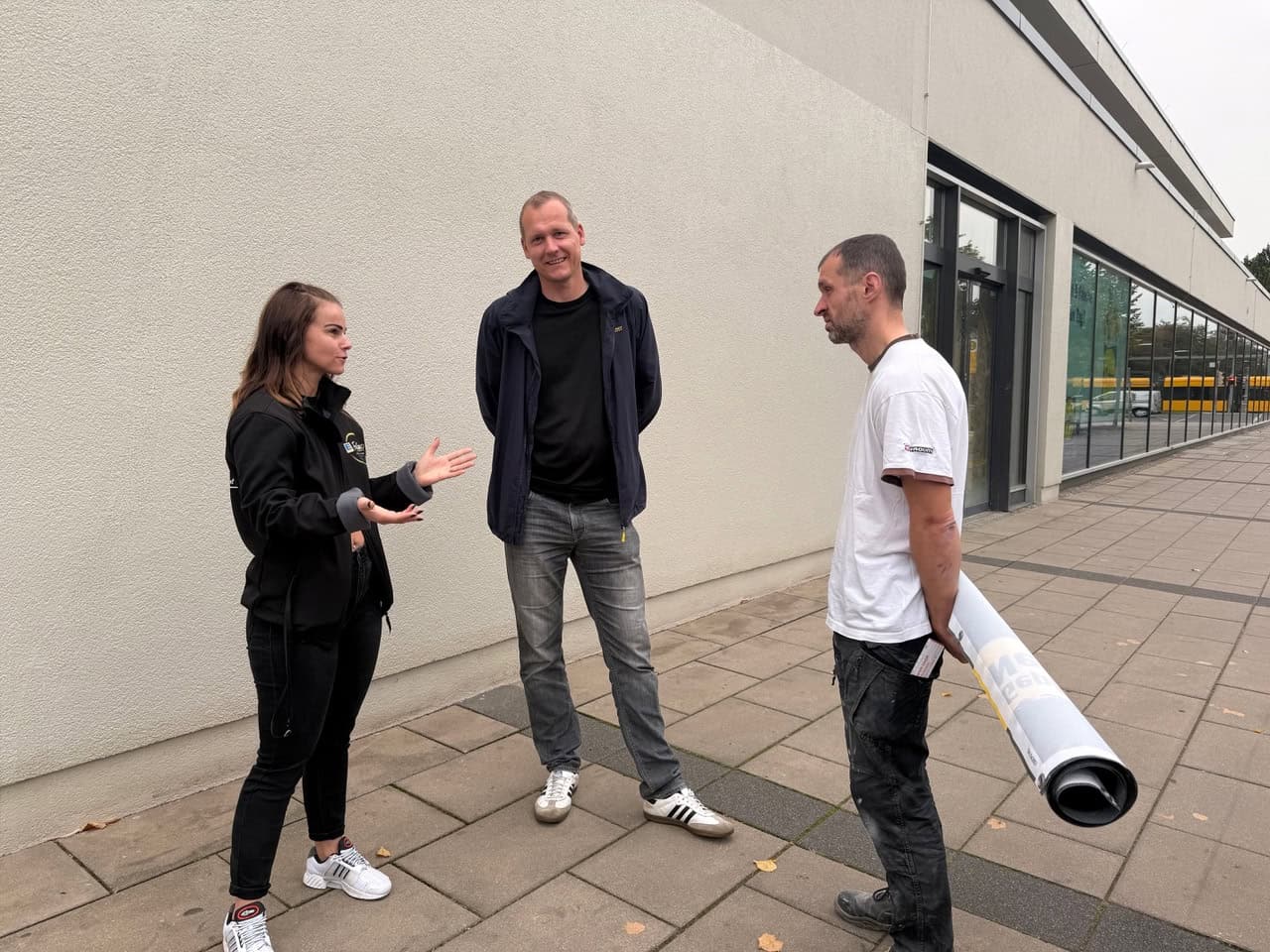 Michaela Felsch, Tobias Schmidt und Maik Pasche vor dem neuen Edeka-Markt in Dresden Michaela Felsch gestikuliert im Gespräch mit zwei Männern vor der Außenwand und der Glasfront des neuen Supermarkts am Pirnaischen Platz. Ein Mann hält ein zusammengerolltes Banner unter dem Arm.