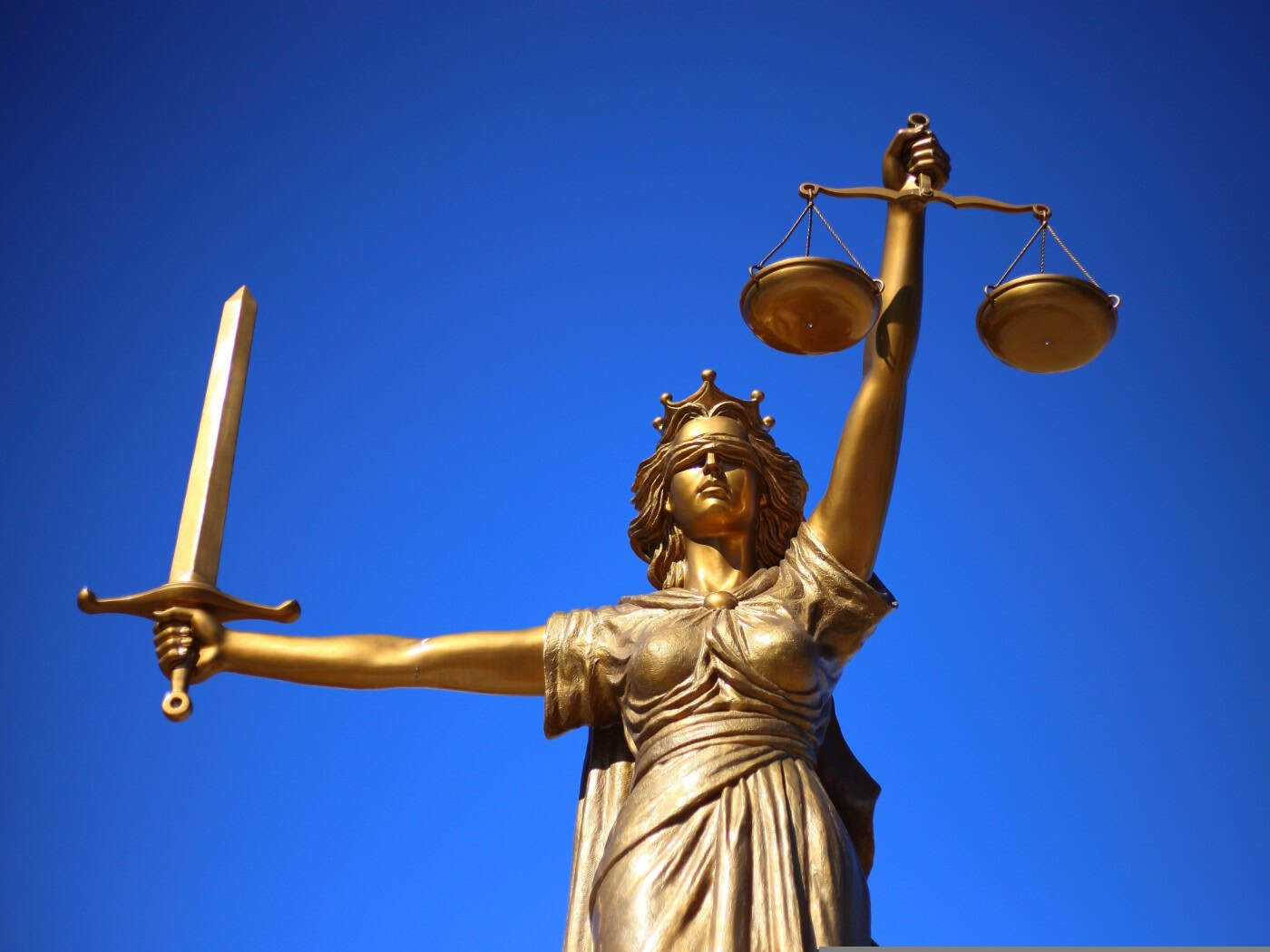 Symbolbild: Goldene Statue der Justitia mit verbundenen Augen, Waagschale in der erhobenen linken und Schwert in der rechten Hand vor strahlend blauem Himmel. Sie steht sinnbildlich für die Anklage im Fall der transfeindlichen Attacke in Dresden.