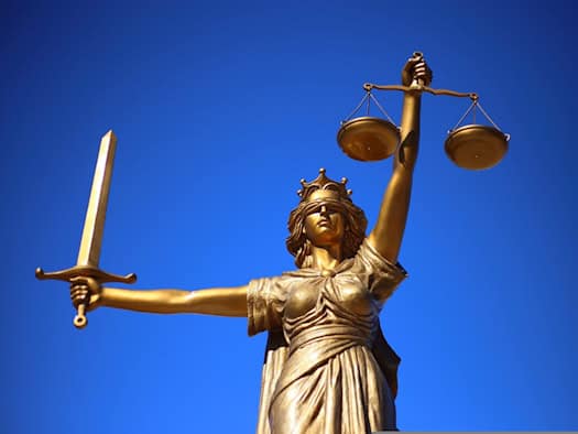 Symbolbild: Goldene Statue der Justitia mit verbundenen Augen, Waagschale in der erhobenen linken und Schwert in der rechten Hand vor strahlend blauem Himmel. Sie steht sinnbildlich für die Anklage im Fall der transfeindlichen Attacke in Dresden.