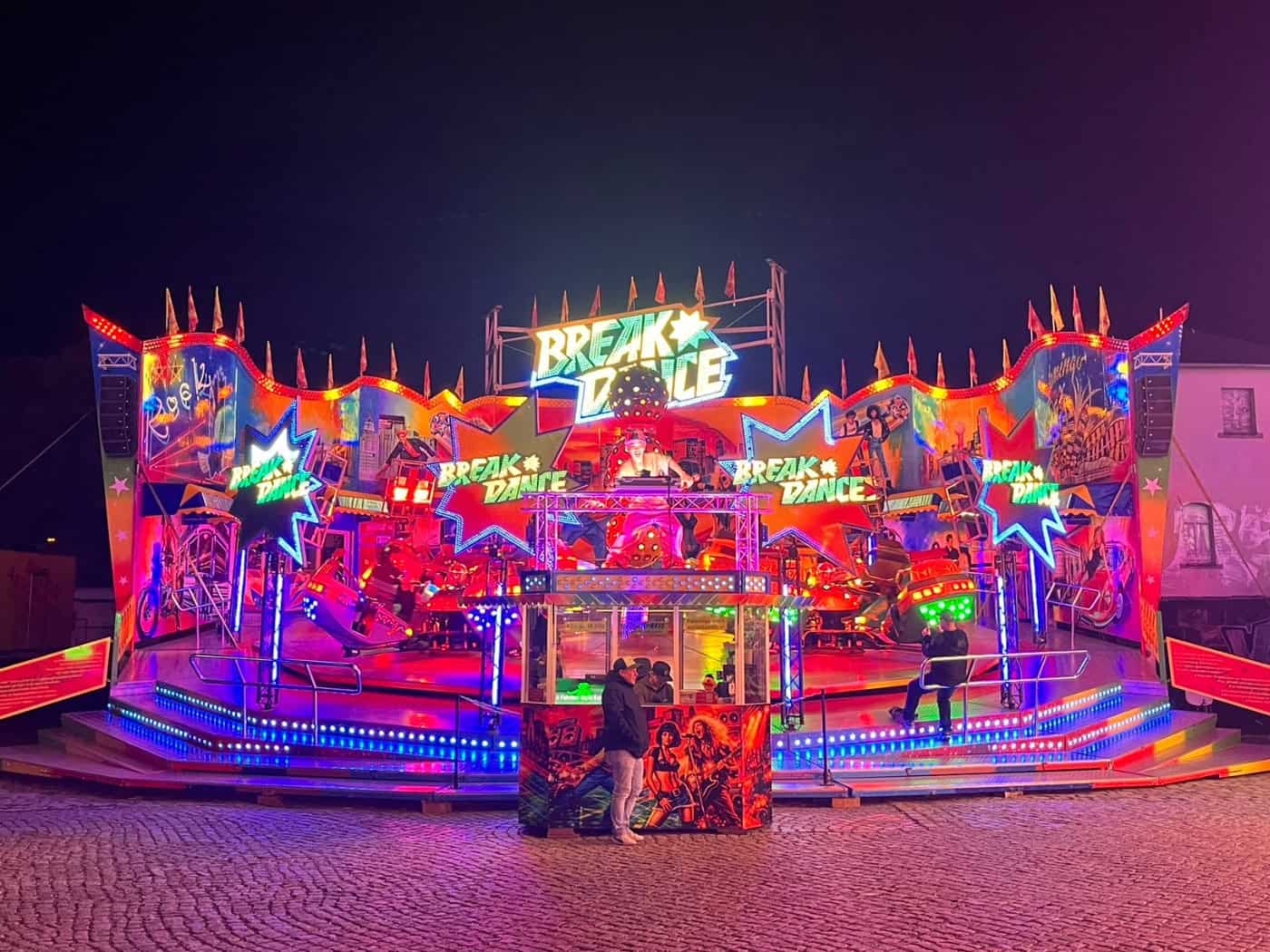 Nächtliche Ansicht des bunten Fahrgeschäfts „Break Dancer“ auf dem Herbstvolksfest an der Pieschener Allee in Dresden. Die Attraktion leuchtet in bunten Farben vor dunklem Nachthimmel auf dem gepflasterten Festplatz.
