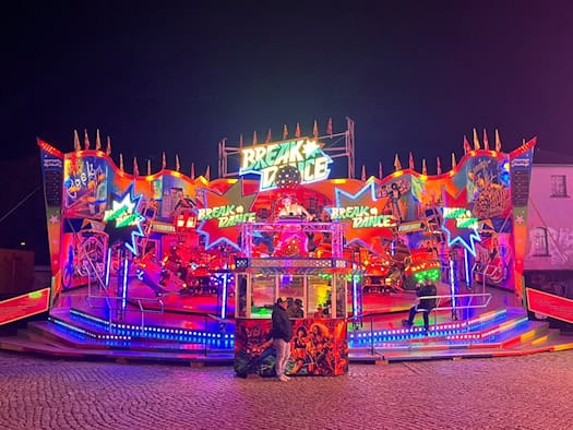 Nächtliche Ansicht des bunten Fahrgeschäfts „Break Dancer“ auf dem Herbstvolksfest an der Pieschener Allee in Dresden. Die Attraktion leuchtet in bunten Farben vor dunklem Nachthimmel auf dem gepflasterten Festplatz.