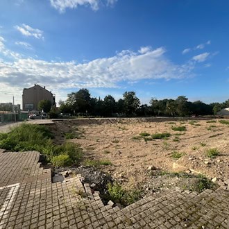 Eine große, beräumte Sandfläche mit vereinzeltem Grün unter blauem Himmel. Im Vordergrund gepflasterter Boden, im Hintergrund Bäume und Gebäude. Es handelt sich um das Bauareal der ehemaligen Operette in Dresden-Leuben.