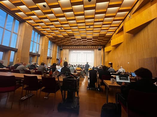 Blick von hinten in den mit Holz verkleideten Plenarsaal des Dresdner Rathauses. Die Stadträte sitzen an ihren Tischen mit Laptops, im Hintergrund ist das Podium mit Präsentationsleinwand sowie den Flaggen von Deutschland und Sachsen zu sehen.