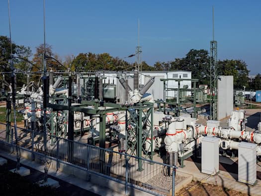 Außenanlage des Umspannwerks Räcknitz in Dresden mit silbrigen Schaltanlagen, hochragenden Isolatoren und Transformatoren auf einem eingefassten Areal vor blauem Himmel.