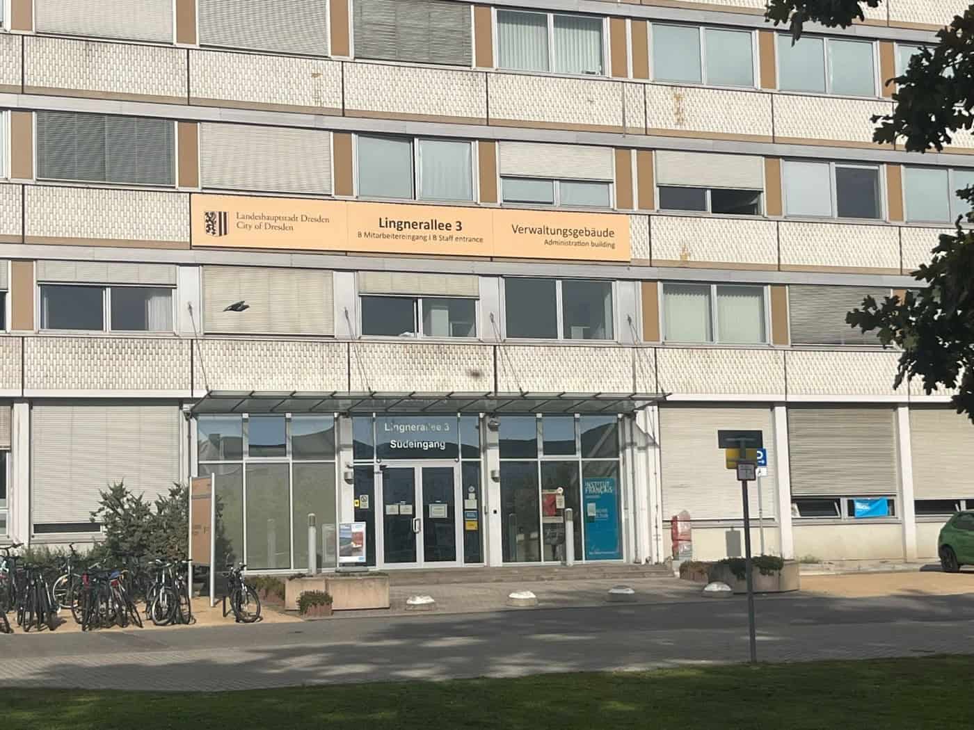 Außenansicht des Verwaltungsgebäudes der Landeshauptstadt Dresden an der Lingnerallee 3 mit Südeingang, Glasfassade im Erdgeschoss und großem Schild über dem Eingangsbereich.