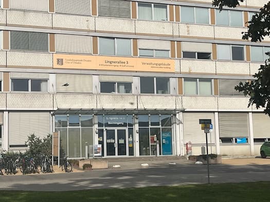 Außenansicht des Verwaltungsgebäudes der Landeshauptstadt Dresden an der Lingnerallee 3 mit Südeingang, Glasfassade im Erdgeschoss und großem Schild über dem Eingangsbereich.