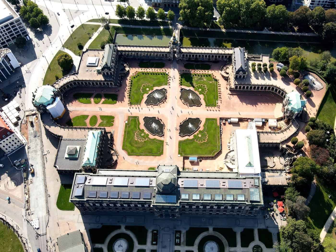 Senkrechte Luftaufnahme des barocken Dresdner Zwingers mit seinem symmetrischen Innenhof, Wegen, Rasenflächen und Brunnenanlagen. Oben ist das Kronentor zu sehen, im Vordergrund befindet sich die Sempergalerie mit der Porzellansammlung.