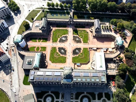 Senkrechte Luftaufnahme des barocken Dresdner Zwingers mit seinem symmetrischen Innenhof, Wegen, Rasenflächen und Brunnenanlagen. Oben ist das Kronentor zu sehen, im Vordergrund befindet sich die Sempergalerie mit der Porzellansammlung.