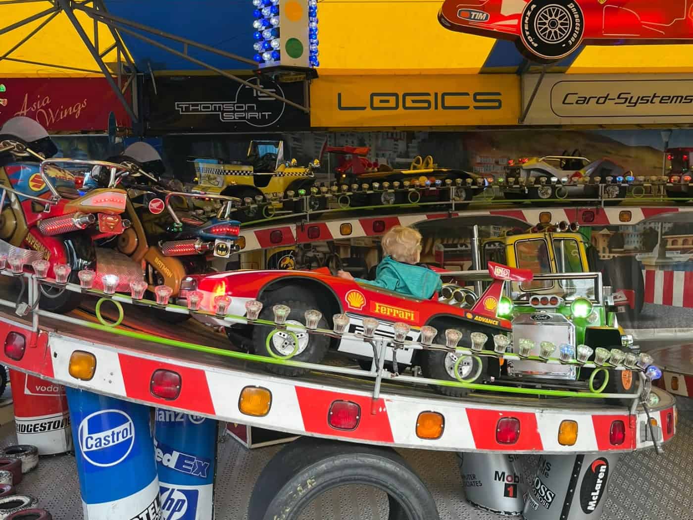 Blick auf ein buntes Kinderkarussell beziehungsweise einen Autoscooter auf dem Dresdner Herbstfest mit kleinen Rennauto-Fahrzeugen, bunten Deko-Elementen, Reifen-Applikationen und bunten Dachplanen.