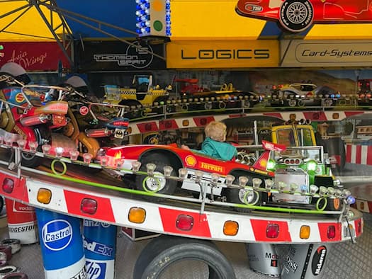 Blick auf ein buntes Kinderkarussell beziehungsweise einen Autoscooter auf dem Dresdner Herbstfest mit kleinen Rennauto-Fahrzeugen, bunten Deko-Elementen, Reifen-Applikationen und bunten Dachplanen.