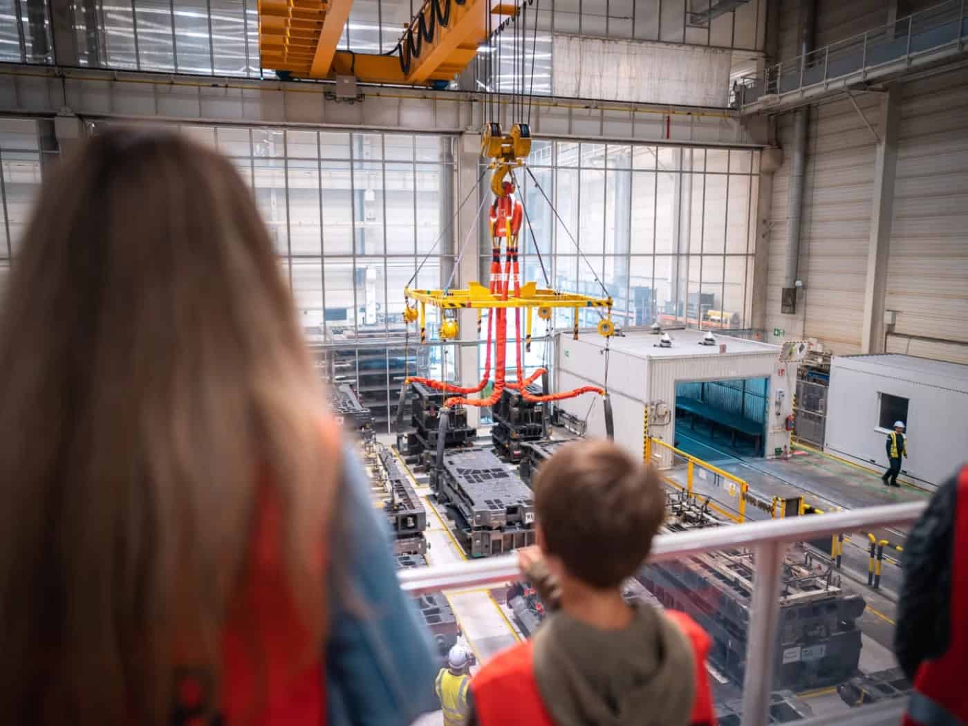 Junge Besucher blicken bei einer Werksführung im Toyota-Werk in Kolín von einer Galerie auf eine Produktionshalle mit Industriekran und Fertigungsanlagen.