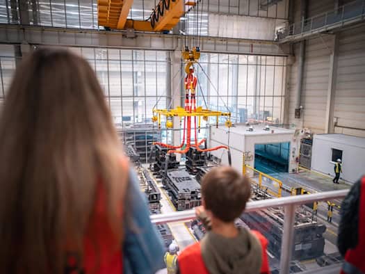 Junge Besucher blicken bei einer Werksführung im Toyota-Werk in Kolín von einer Galerie auf eine Produktionshalle mit Industriekran und Fertigungsanlagen.