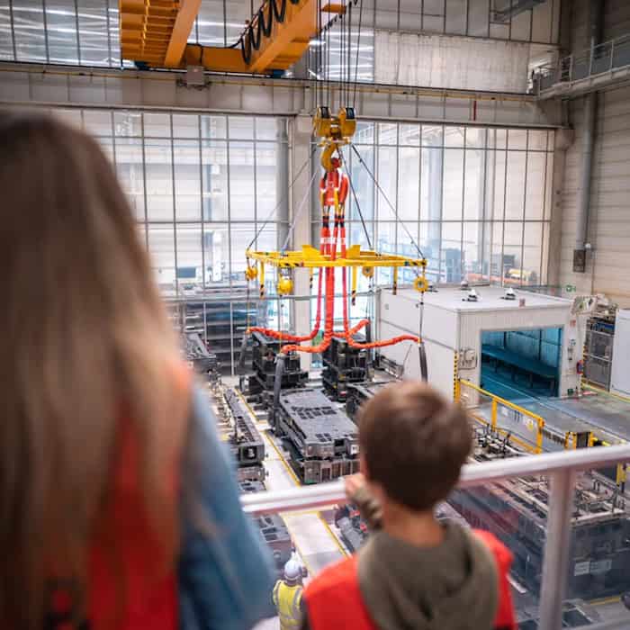 Junge Besucher blicken bei einer Werksführung im Toyota-Werk in Kolín von einer Galerie auf eine Produktionshalle mit Industriekran und Fertigungsanlagen.