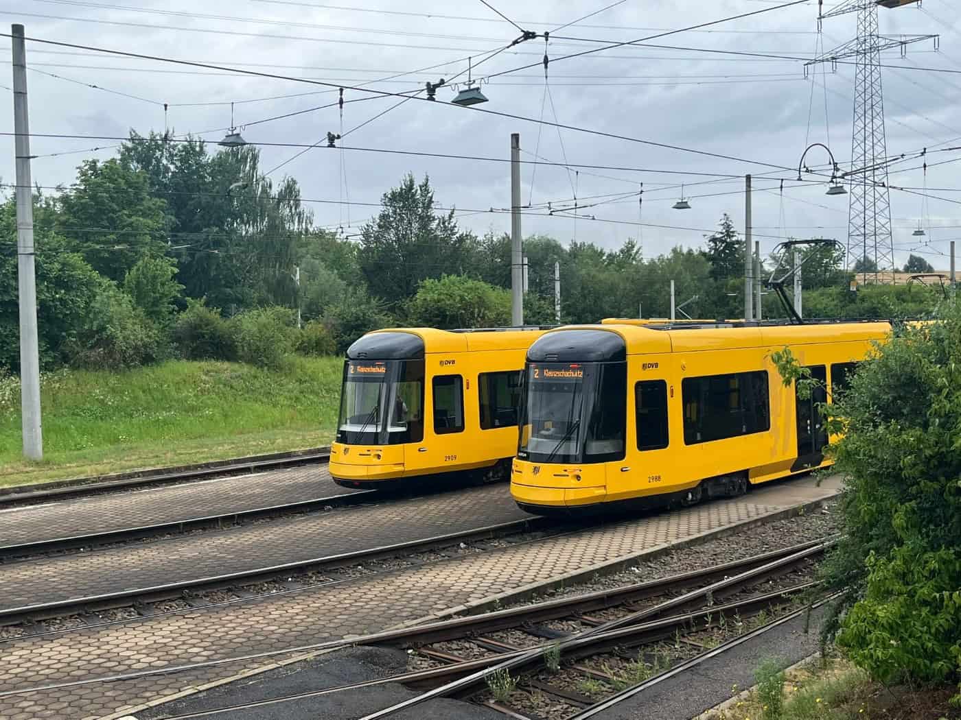 Zwei gelbe Straßenbahnen der Dresdner Verkehrsbetriebe (DVB) stehen nebeneinander auf den Gleisen im Betriebshof Gorbitz. Im Hintergrund sind Bäume und ein Strommast unter bedecktem Himmel zu sehen.