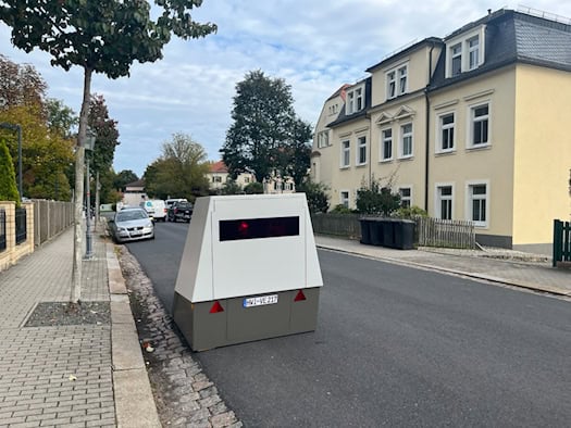 Ein weiß-grauer Blitzer-Messanhänger mit dem Nummernschild HWI-VE 217 steht am Rand der Schützenhofstraße in Dresden vor Wohnhäusern und kontrolliert die Tempo-30-Zone.