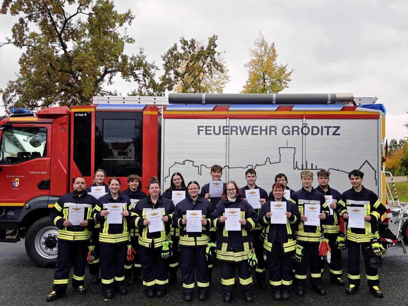 Gruppe von Feuerwehrleuten mit Urkunden vor einem Löschfahrzeug der Feuerwehr Gröditz