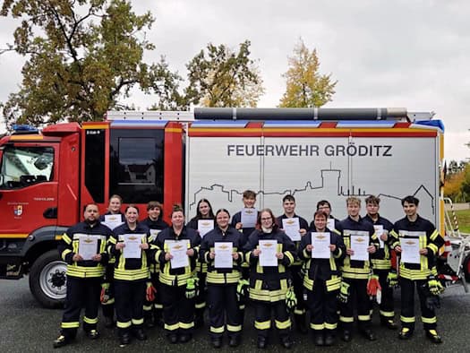 Gruppe von Feuerwehrleuten mit Urkunden vor einem Löschfahrzeug der Feuerwehr Gröditz