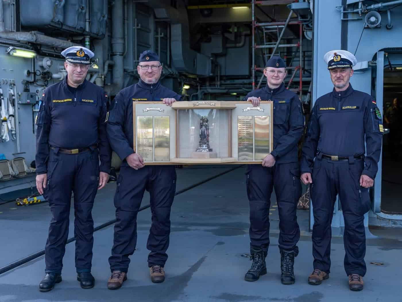 Vier Marinesoldaten an Deck der Fregatte Sachsen halten die Plakette des Barbarapreises