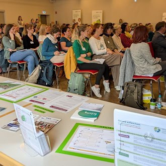 Zuhörerinnen und Zuhörer beim Kita-Fachtag im Saal des Alberttreffs Großenhain, vorn ein Tisch mit Infomaterial