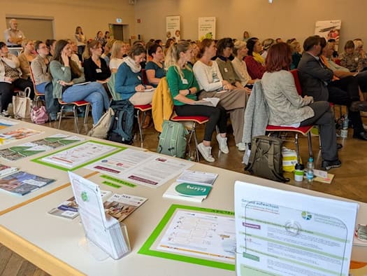 Zuhörerinnen und Zuhörer beim Kita-Fachtag im Saal des Alberttreffs Großenhain, vorn ein Tisch mit Infomaterial