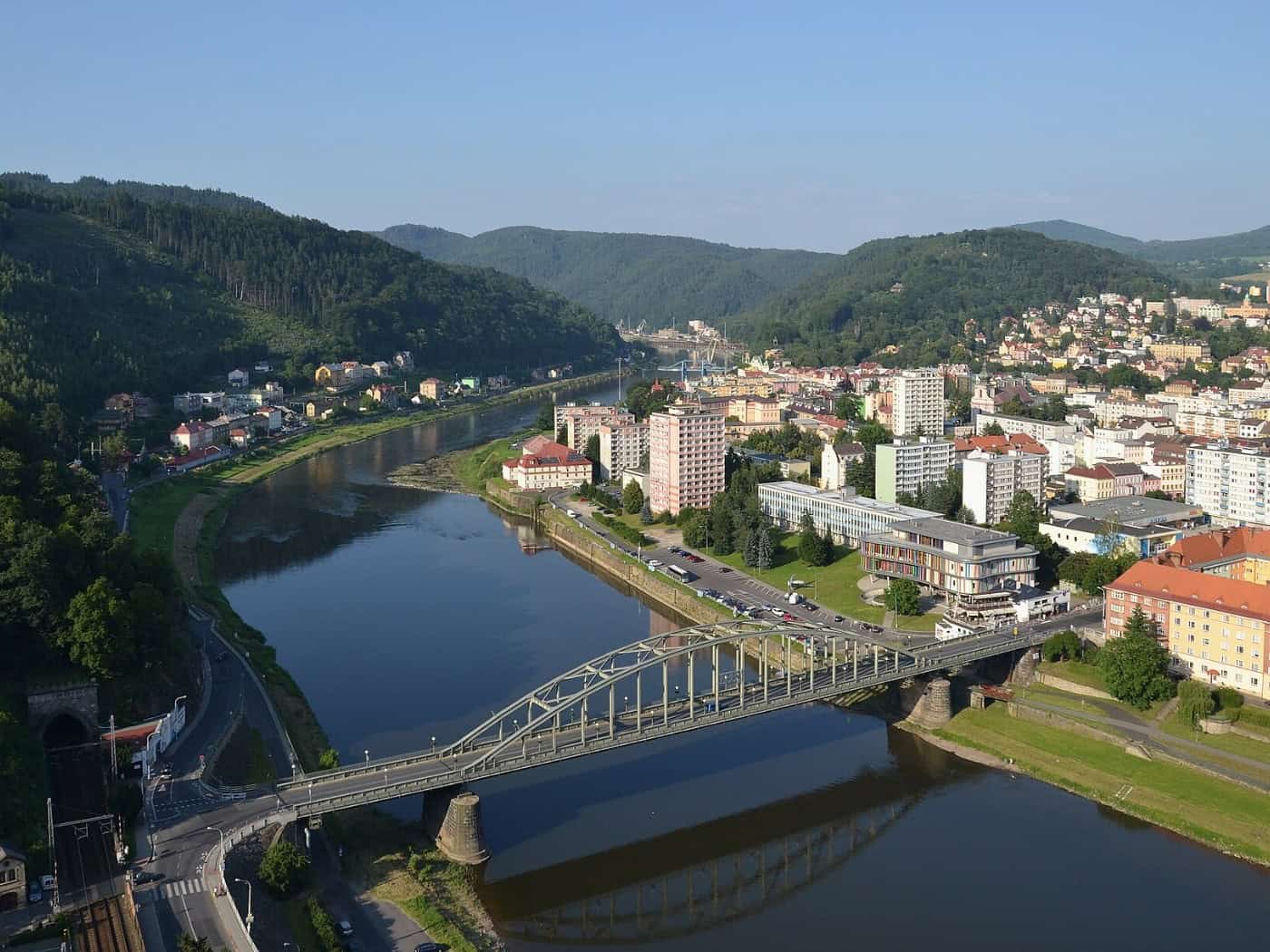 Blick von oben auf die Elbe in Děčín mit Brücke, Uferstraßen und bewaldeten Hängen