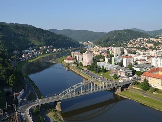 Blick von oben auf die Elbe in Děčín mit Brücke, Uferstraßen und bewaldeten Hängen