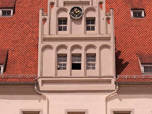 Ziergiebel mit Uhr am Meißner Rathaus, darunter Fenster mit roten Blumenkästen