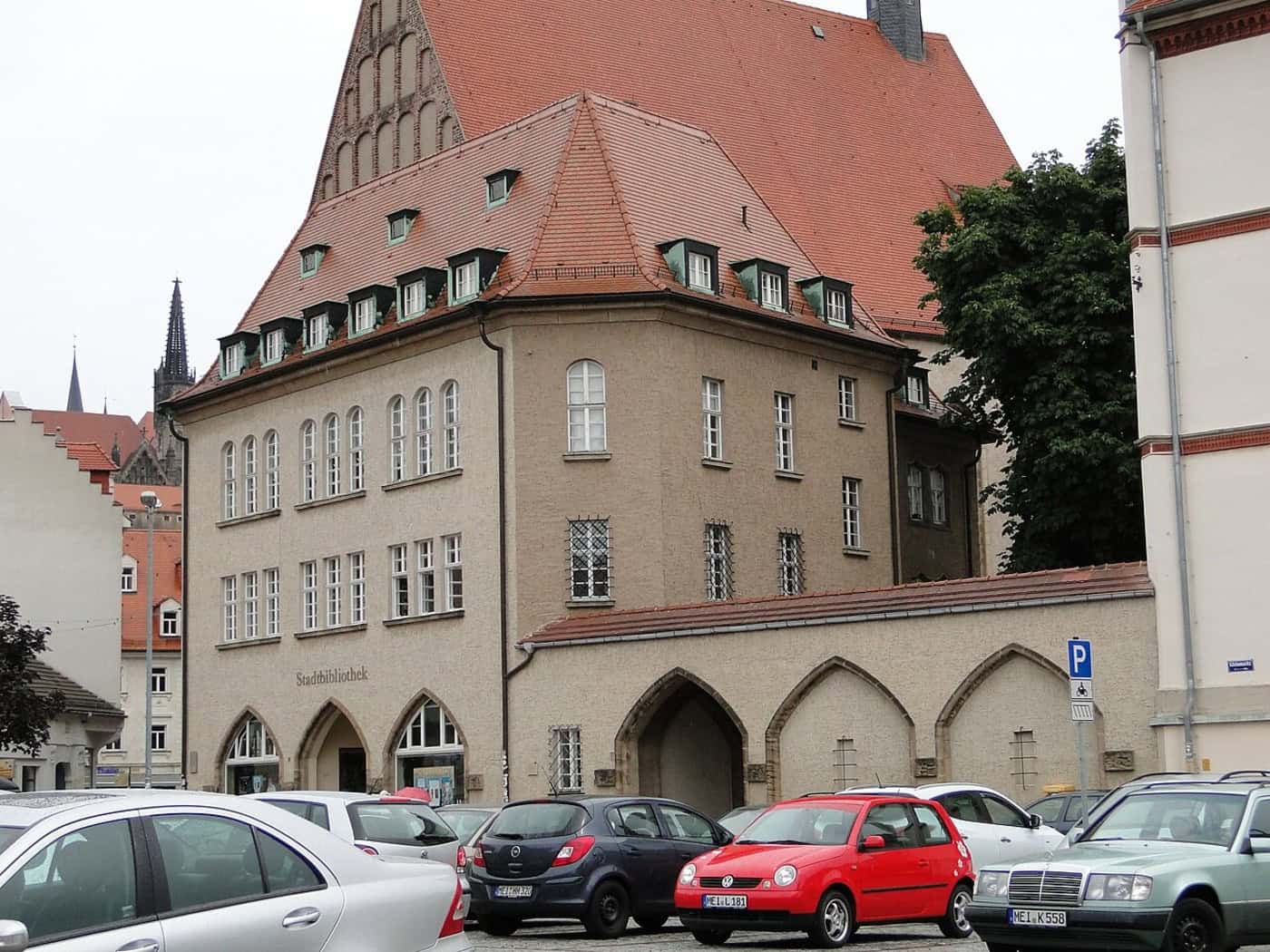 Das Gebäude der Stadtbibliothek Meißen am Kleinmarkt mit rotem Ziegeldach, Schriftzug „Stadtbibliothek“ und Spitzbogenarkaden, davor parkende Autos