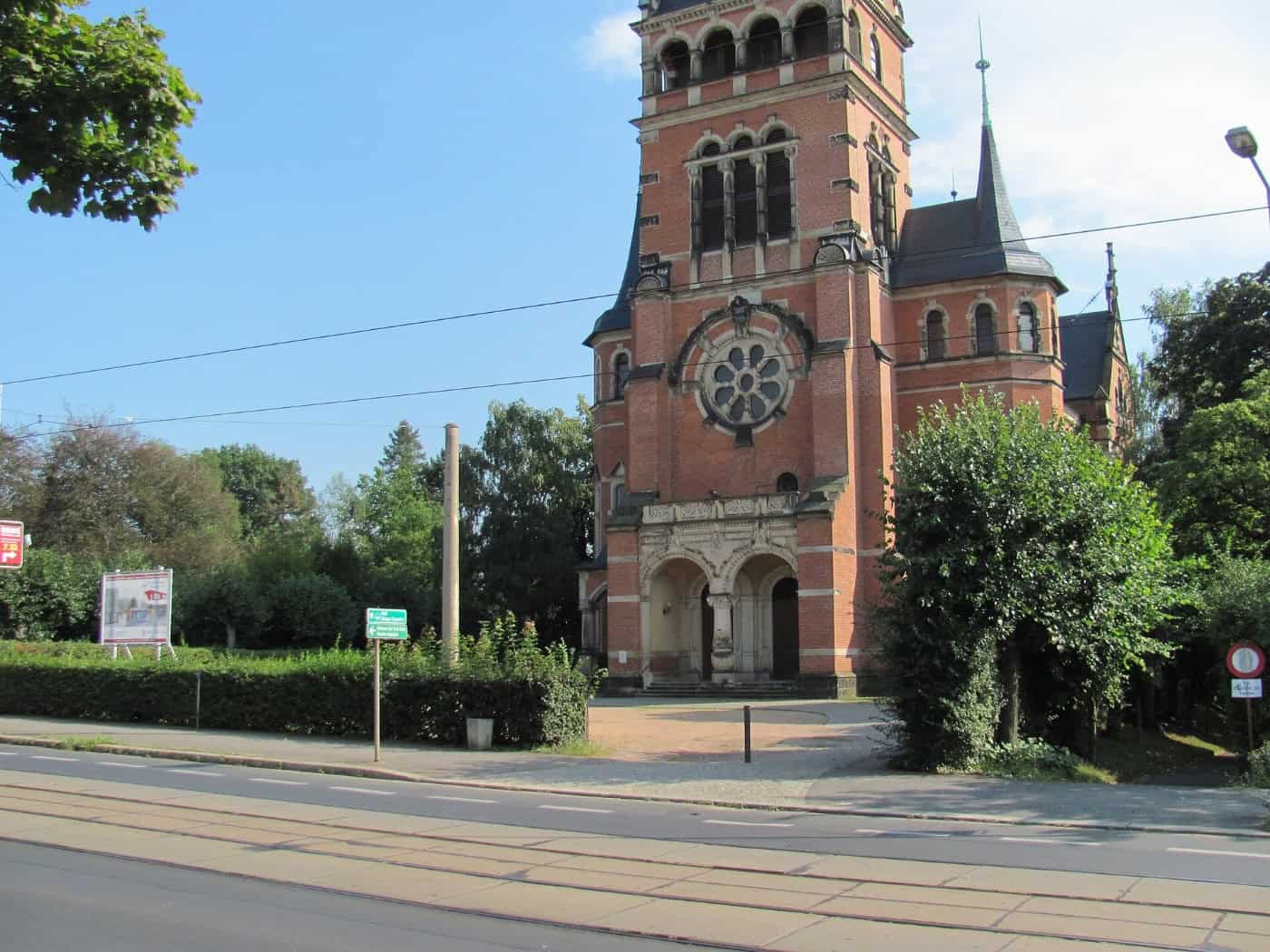 Backsteinkirche mit hohem Turm und Rosettenfenster an einer Straße in Radebeul-Ost