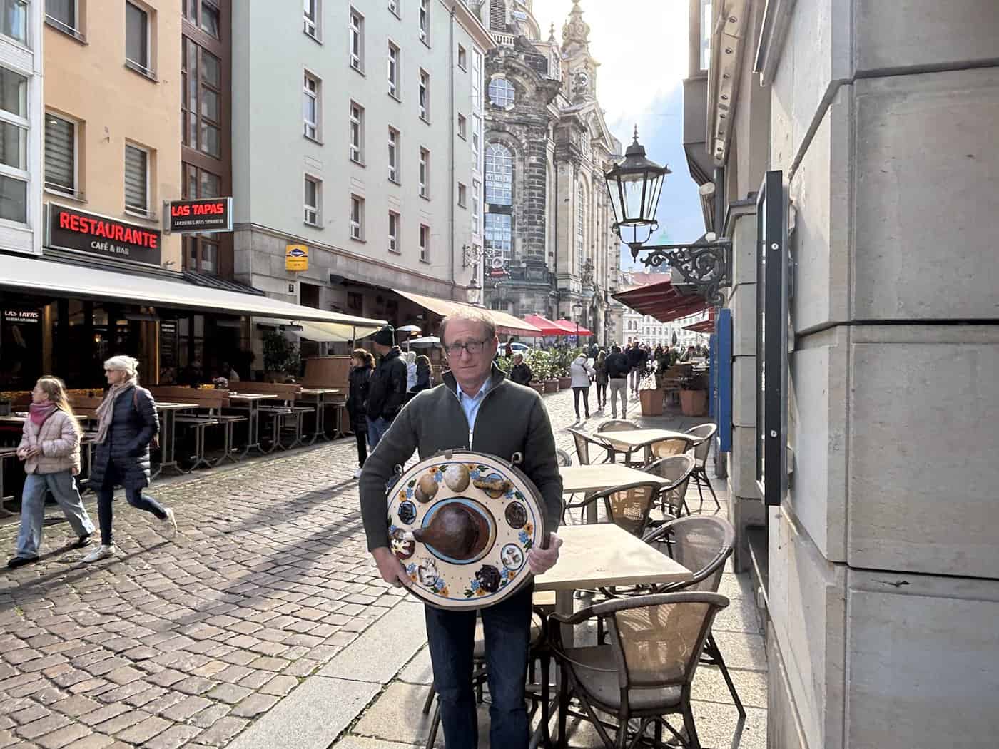 Matthias Singer steht in einer Dresdner Altstadtgasse nahe der Frauenkirche und hält das kunstvoll gestaltete Ladenschild für sein neues Restaurant „Zum Neinerlaa“.