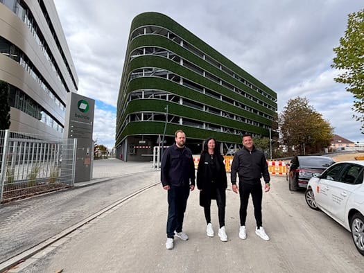 Raphael Marquardt, Lydia Förster und Andreas Bergermann stehen vor einem mehrstöckigen, rund geschwungenen Parkhaus mit grüner Moosverkleidung an den Außenrängen. Links steht ein Firmenstele mit der Aufschrift „bechtle“.