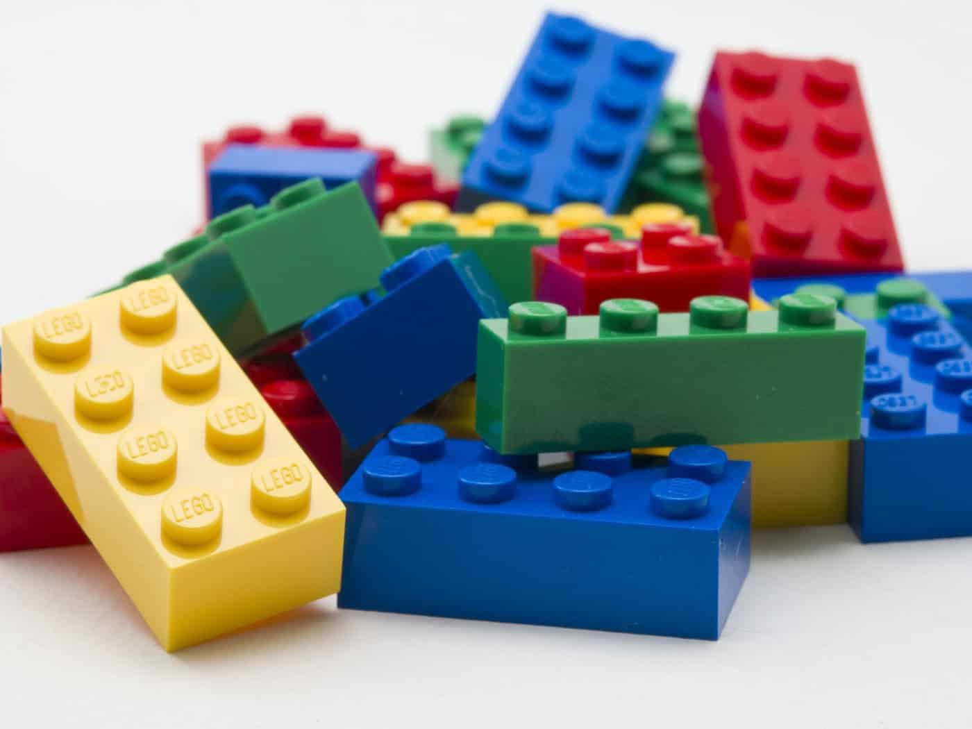 Lose LEGO-Steine in Rot, Gelb, Grün und Blau auf einer hellen Fläche.