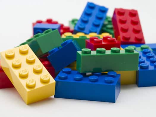 Lose LEGO-Steine in Rot, Gelb, Grün und Blau auf einer hellen Fläche.