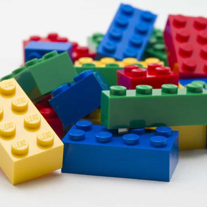 Lose LEGO-Steine in Rot, Gelb, Grün und Blau auf einer hellen Fläche.