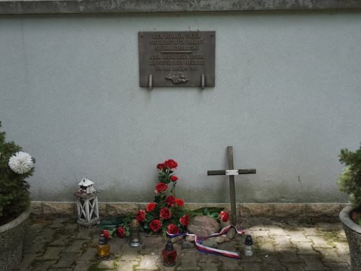 Deutsch-tschechische Gedenktafel in Postoloprty mit Blumen, Kerzen und einem Holzkreuz.