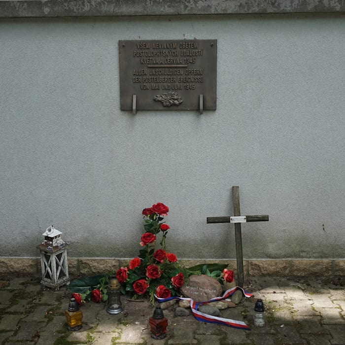 Deutsch-tschechische Gedenktafel in Postoloprty mit Blumen, Kerzen und einem Holzkreuz.