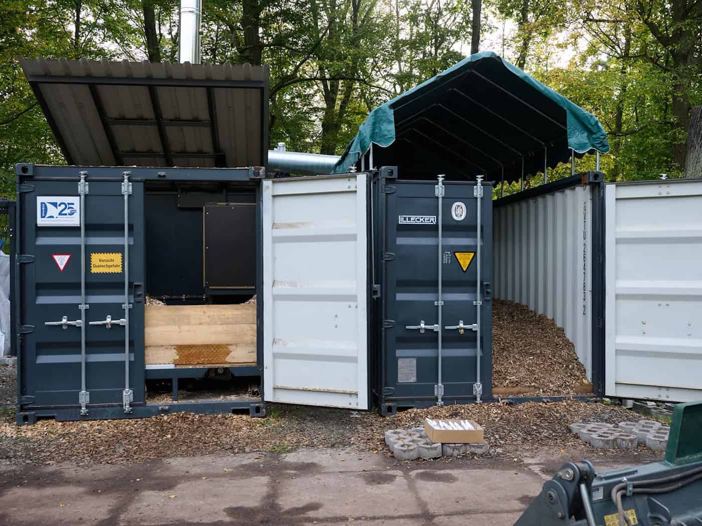 Autarke Pyrolyseanlage zur Pflanzenkohle-Gewinnung in Dresden Gesamtansicht der zwei dunklen Container-Einheiten im Großen Garten Dresden: Links befindet sich die Pyrolyseanlage, rechts der Trocknungscontainer für Holzhackschnitzel.