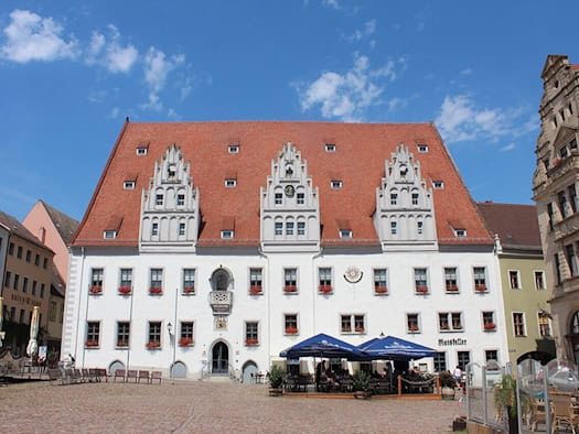 Weißes Rathaus Meißen mit rotem Dach und drei Ziergiebeln am Marktplatz, davor Sonnenschirme eines Lokals