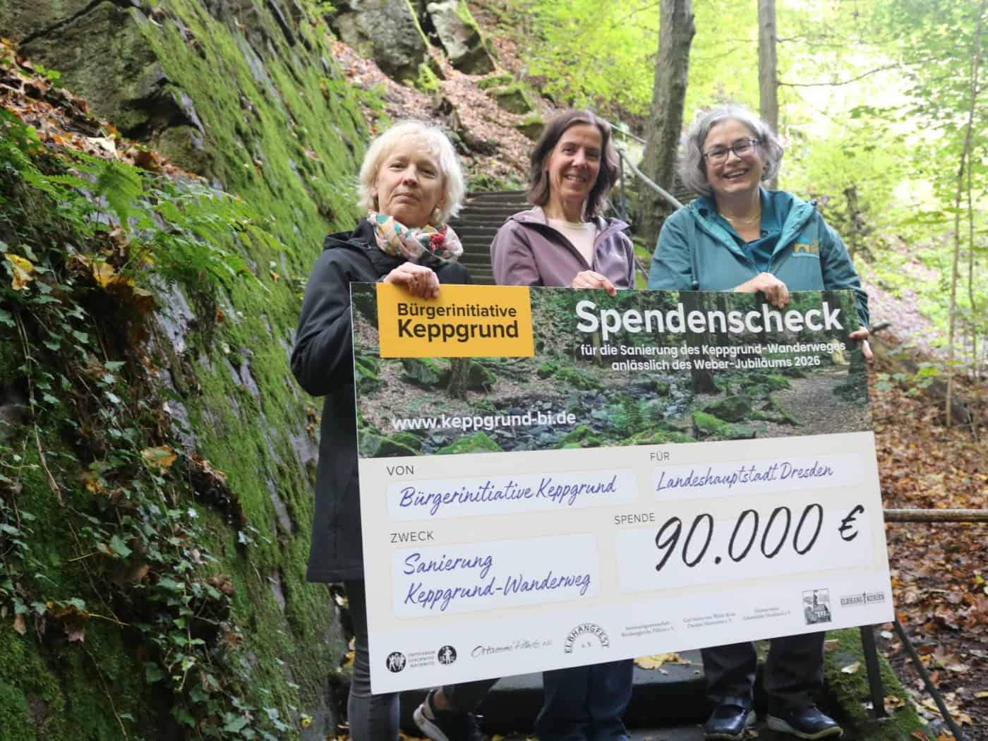 Drei Frauen – Simone Prüfer, Manuela Schreiter und Eva Jähnigen (v.l.) – stehen lächelnd auf einer Steintreppe im Keppgrund und halten gemeinsam einen großen Spendenscheck der Bürgerinitiative über 90.000 Euro in die Kamera.