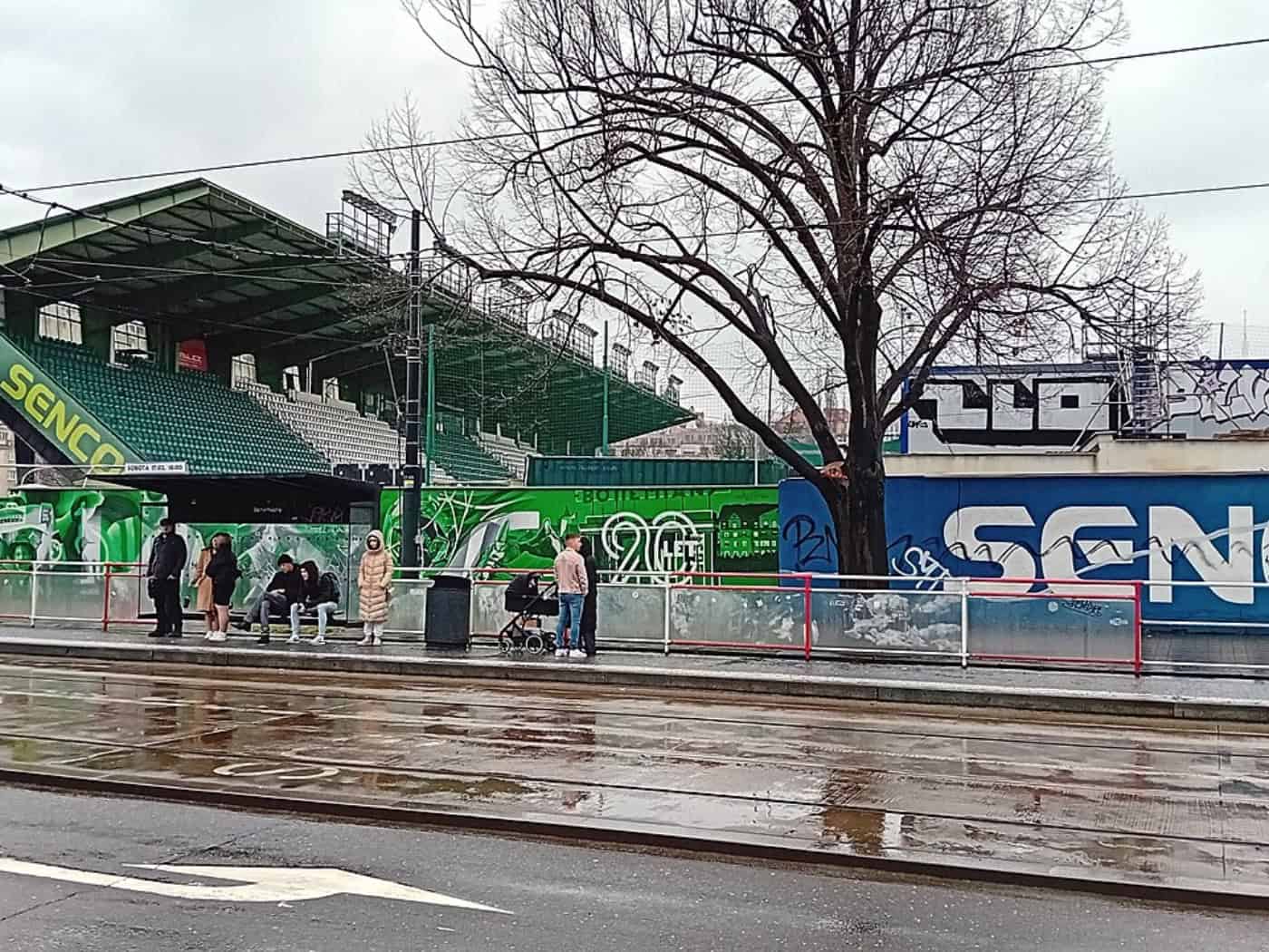 Blick von der Straßenbahnhaltestelle auf die grüne Tribüne und die Außenmauer des Stadions Ďolíček in Prag.