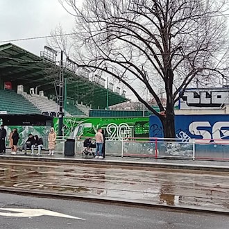 Blick von der Straßenbahnhaltestelle auf die grüne Tribüne und die Außenmauer des Stadions Ďolíček in Prag.