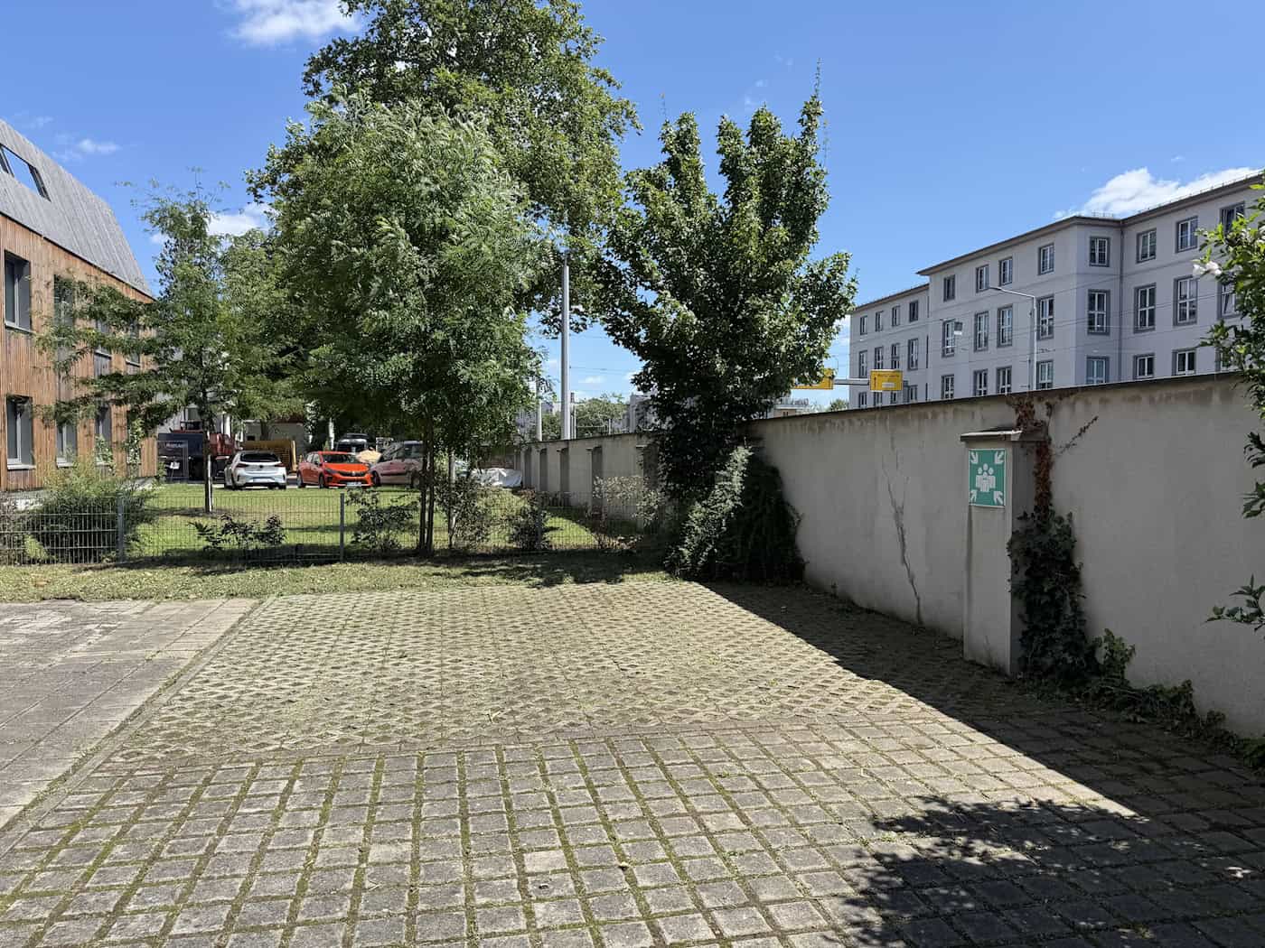 Hof- und Parkbereich mit gepflasterten Stellplätzen auf dem Grundstück der Villa an der Bautzner Straße, umgeben von Grünflächen, Bäumen und einer hohen weiß verputzten Mauer.