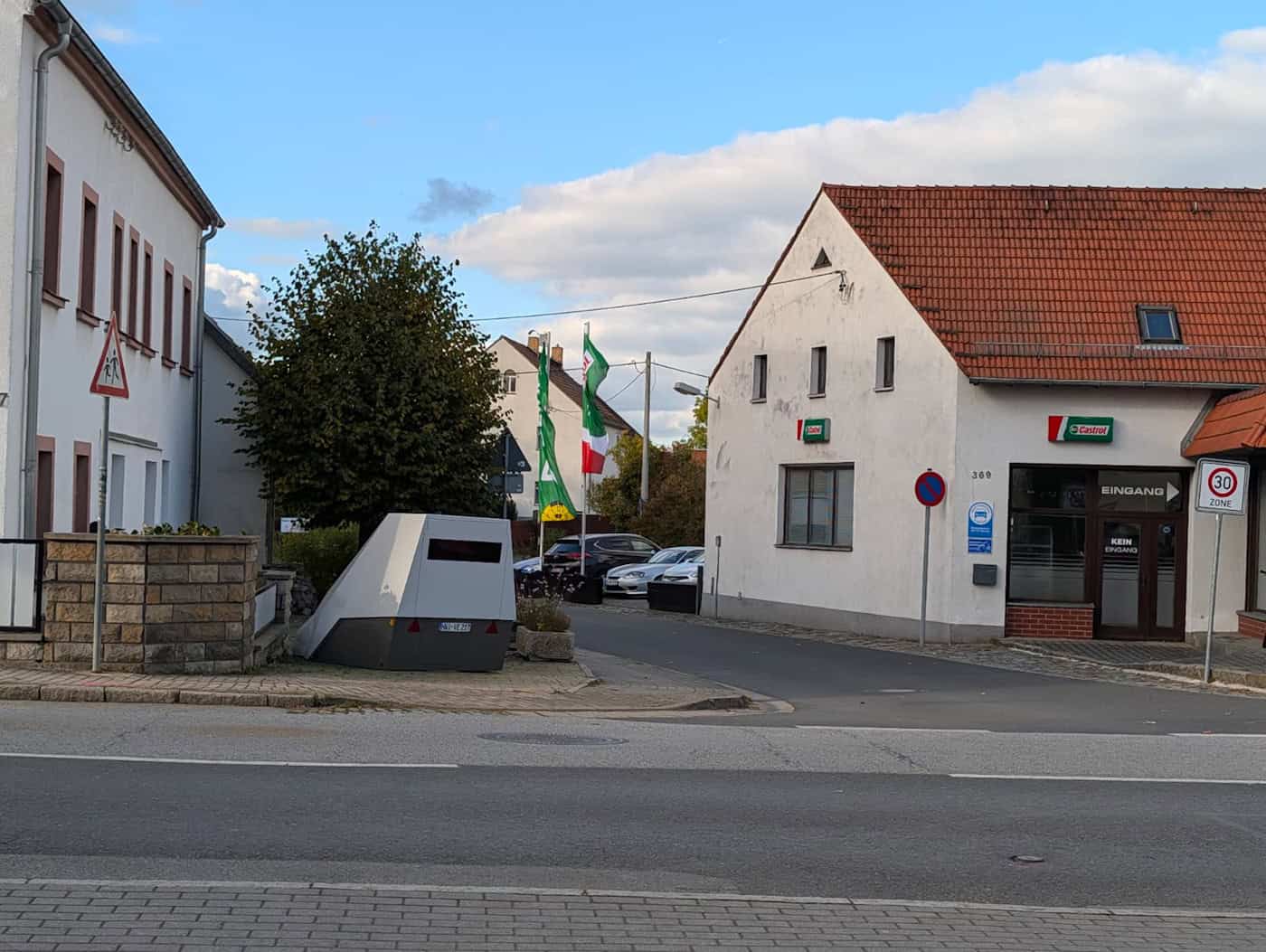 Der Superblitzer (Enforcement Trailer) steht an der Königsbrücker Landstraße in Weixdorf. Der graue mobile Blitzer-Anhänger (Enforcement Trailer) steht am Fahrbahnrand an einer Kreuzung in Dresden-Weixdorf; im Hintergrund sind weiße Wohnhäuser, parkende Autos und eine 30-Zone-Verkehrstafel zu sehen.