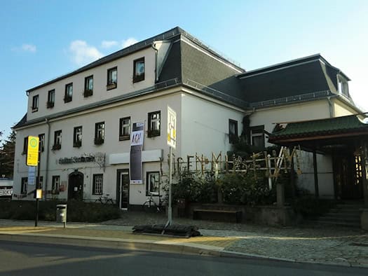 Weißes zweistöckiges Gasthaus mit Mansarddach, davor ein großer Schriftzug aus Metallbuchstaben „Lügenmuseum“ und ein Pavillon mit grünem Dach